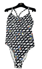 A one-piece swimsuit with a black and white geometric pattern and colorful floral accents, hanging on a black hanger with a Chanel logo, placed on a textured gray fabric surface.
