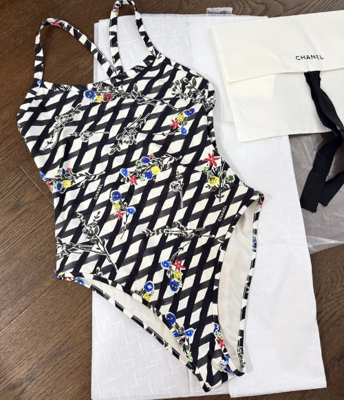 A black and white patterned one-piece swimsuit laid flat on a white surface, with a small black-and-white accessory visible at the side.