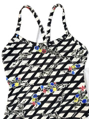 A black and white geometric patterned halter top with colorful floral embroidery, laid flat on a wooden surface next to a white Chanel bag.