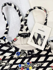 A black and white patterned pet collar with a matching fabric tag, displayed on a white surface with a black and white patterned fabric underneath.