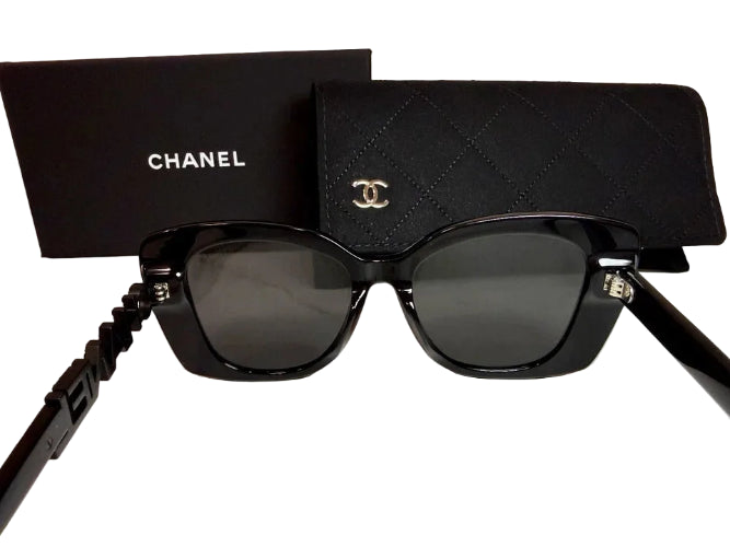 Chanel black sunglasses with dark lenses, shown with a black Chanel box and matching quilted black case on a light marble surface.