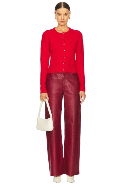 Person wearing a red cardigan and red pants holding a white handbag on a white background
