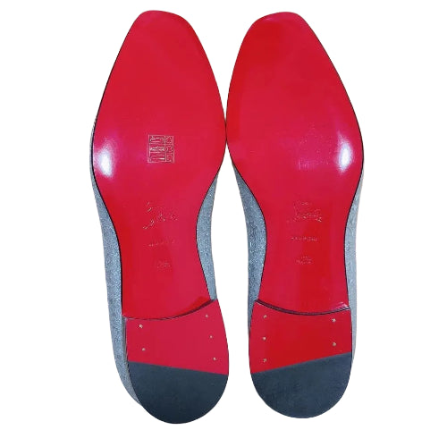 Red soles of shoes with a gray insole on a wooden floor, with a Louis Vuitton box in the background.