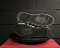 Black shoes with soles facing up on a red surface against a dark brick wall.