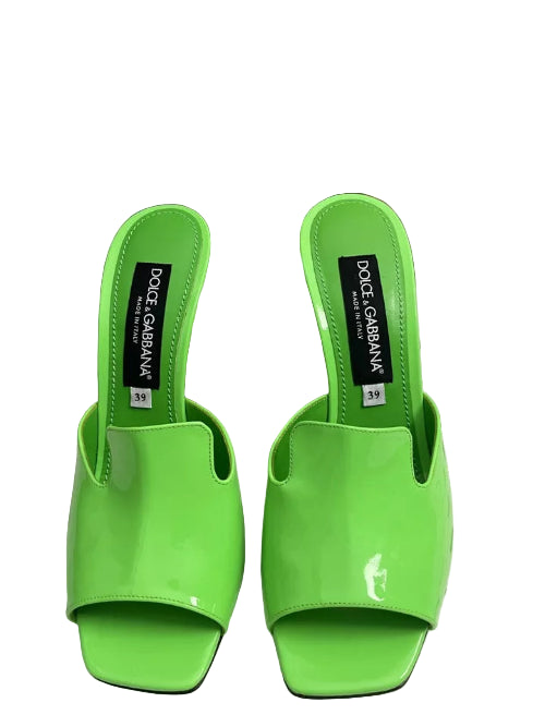 Pair of green Dolce & Gabbana shoes on a metal surface with a colorful background.