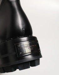 Close-up of a black leather boot with a chunky lug sole and a silver-tone metal plaque engraved with 'DOLCE&GABBANA MILANO ITALY'.