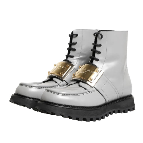 A pair of metallic silver lace-up boots with prominent gold buckle details on the sides and thick black soles, shown against a plain white background.
