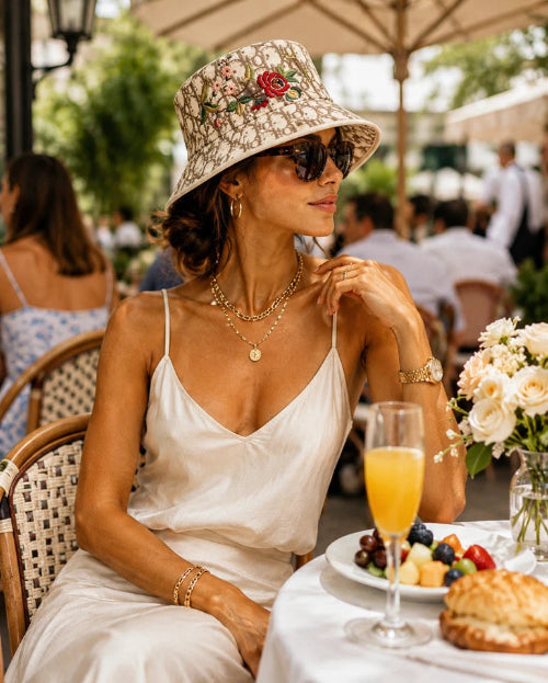 Woman in a white dress and sun hat sitting at an outdoor table with a plate of food.