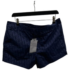 Navy shorts with a brand tag on a hanger against a white brick wall.
