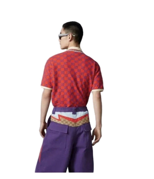A model shown from the back wearing a red short-sleeve t-shirt with a repeating geometric pattern, purple wide-leg trousers, and a patterned waist belt, set against a plain light gray studio background.