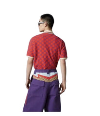A model shown from the back wearing a red short-sleeve t-shirt with a repeating geometric pattern, purple wide-leg trousers, and a patterned waist belt, set against a plain light gray studio background.