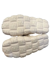 White textured shoes held by a hand against a dark background