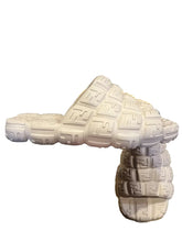 White sandals with a brand logo held by a hand on a gray surface