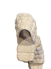 Beige sandal with brand logo held by a hand on a dark surface