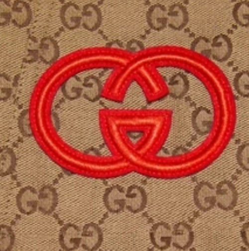 Red Gucci logo patch on a beige fabric background with Gucci logo pattern.