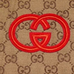 Red Gucci logo patch on a beige fabric background with Gucci logo pattern.