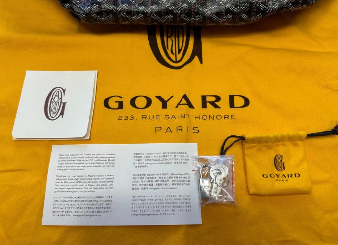 Goyard brand accessories laid out on a yellow Goyard dust bag, including a patterned fabric item at the top, a white Goyard card, an instruction sheet, a small clear plastic bag with metal hardware, and a yellow Goyard drawstring pouch.