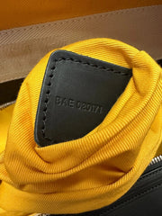 Close-up of a yellow fabric pouch or organizer inside a black bag, showing a black leather tab stamped with the code 'BAE 020171'.