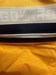 Close-up of a yellow garment with a wide beige woven band featuring embossed GOYARD lettering, a black leather trim, and a silver zipper. GOYARD PARIS branding is visible on the black section.