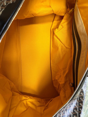 Close-up of the interior of a handbag, showing a bright mustard yellow nylon lining with a side zipper and a patterned fabric exterior corner visible at the bottom right.