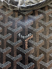 Close-up of a Goyard monogram patterned material with the brand name 'Goyard Honore Se Goyard Paris' printed on it, with a crumpled clear plastic wrap visible at the top.