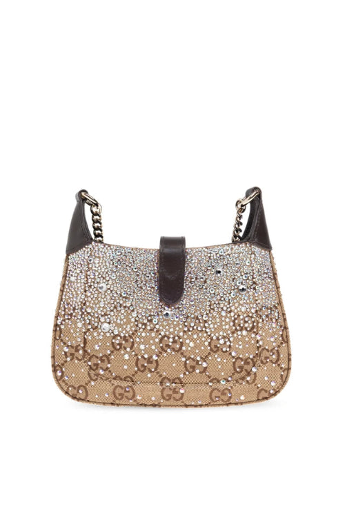 A Gucci monogram canvas shoulder bag in beige and brown, featuring a dark brown leather top handle and side straps, shown against a plain white background.