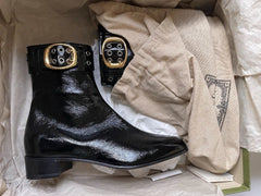 Black shiny boots with gold buckles on a beige surface