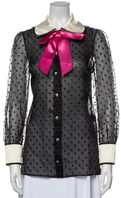 Black polka dot blouse with sheer sleeves and a pink bow on a mannequin against a white background