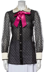 Black polka dot blouse with sheer sleeves and a pink bow on a mannequin against a white background
