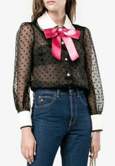 Woman wearing a black lace top with a pink bow, white blouse, and blue jeans.