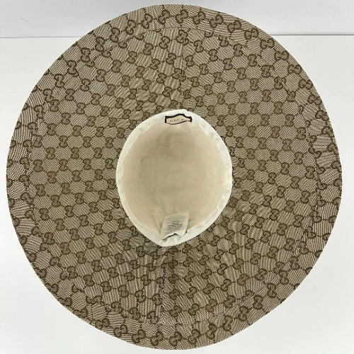 A top-down view of a Gucci hat featuring the signature GG monogram canvas in beige and brown, with a cream-colored inner crown.