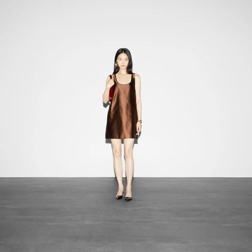 Woman wearing a brown sleeveless dress standing against a plain white background