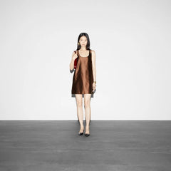 Woman wearing a brown sleeveless dress standing against a plain white background