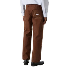 A person shown from the back wearing brown work pants and black shoes against a plain light gray studio background.
