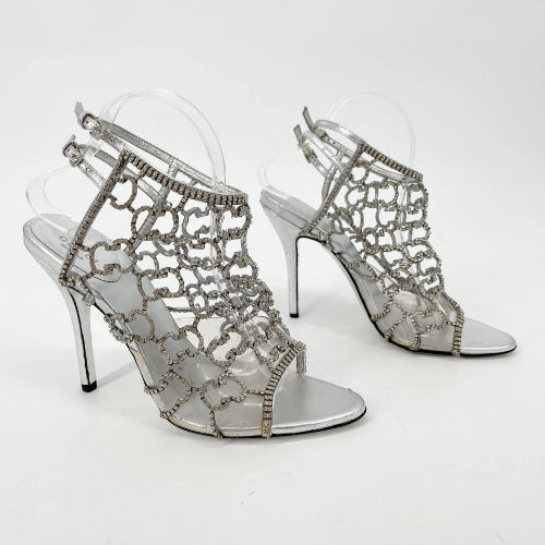 Silver high-heeled shoes with intricate designs on a white background