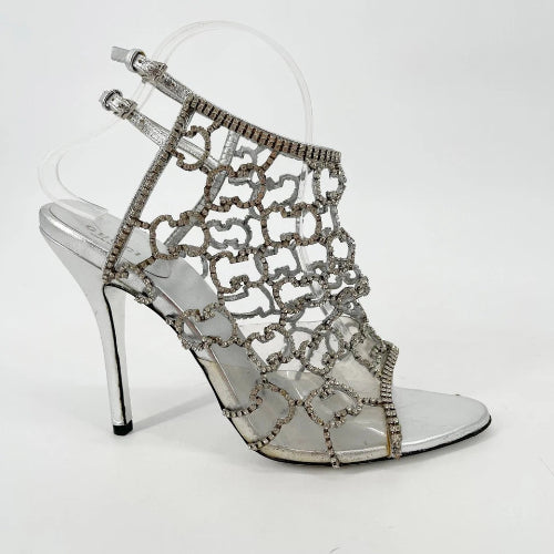 Silver high-heeled shoes with intricate lace design on a clear background
