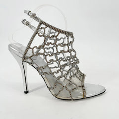 Silver high-heeled shoes with intricate lace design on a clear background