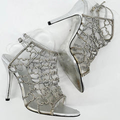 Silver high-heeled shoes with intricate designs on a white background