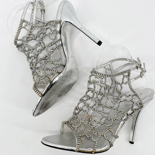 Silver high-heeled shoes with intricate designs on a white background