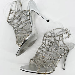 Silver high-heeled shoes with intricate designs on a white background