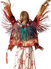 Person wearing a colorful fringed jacket with a white wall background