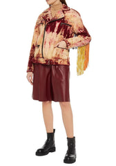 Person wearing a patterned jacket with fringes and leather shorts on a white background