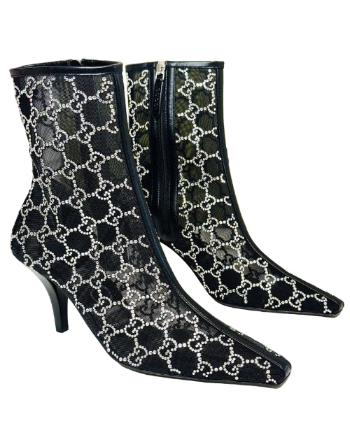 Black high-heeled boots with white pattern on a white surface, Gucci box in the background.