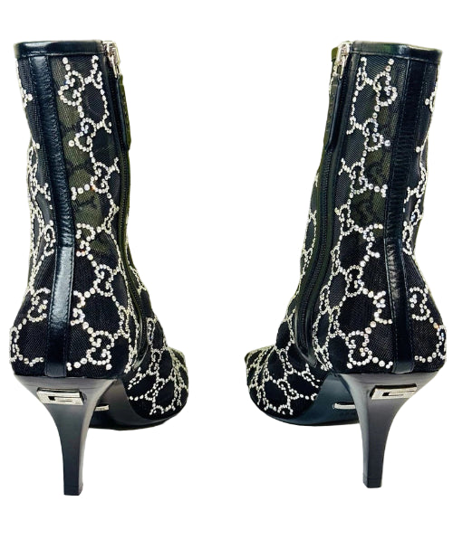 Black high-heeled boots with white pattern on a white surface, Gucci logo in the background.