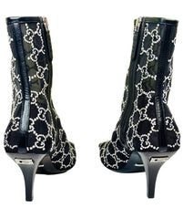 Black high-heeled boots with white pattern on a white surface, Gucci logo in the background.