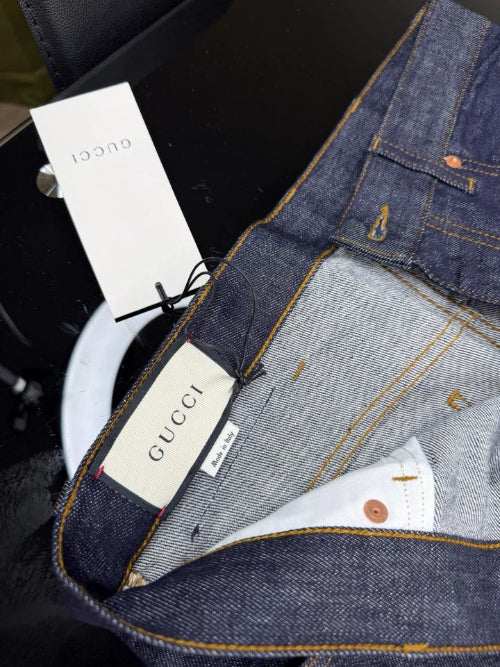 Close-up of Gucci denim jeans showing the inner waistband, interior label, and branded hangtag on a dark surface.