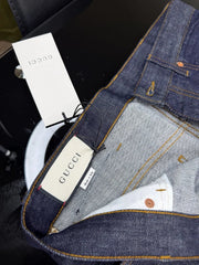 Close-up of Gucci denim jeans showing the inner waistband, interior label, and branded hangtag on a dark surface.