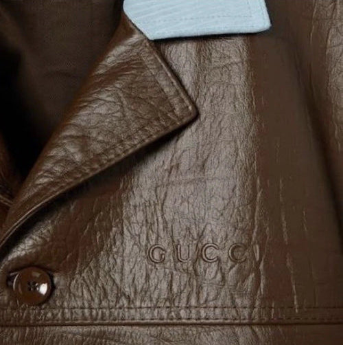 Close-up of a brown leather jacket with 'Gucci' logo and button.