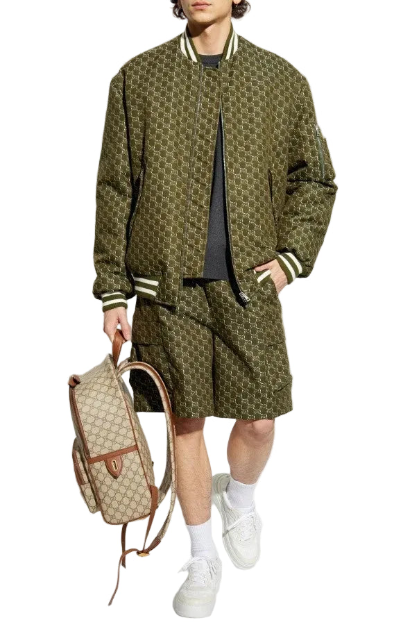 A person wearing an olive green quilted jacket with a matching quilted belt, paired with brown shorts, white sneakers, and a beige shoulder bag.