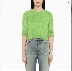 Person wearing a bright green fuzzy sweater and light blue jeans on a white background